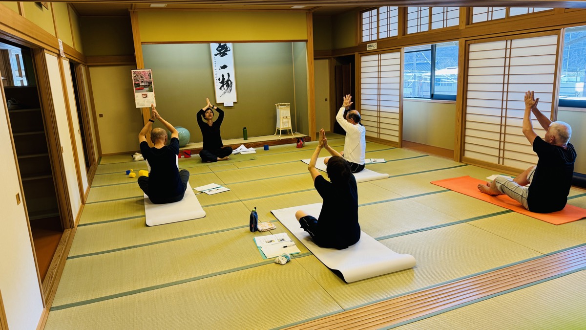 両手を頭上で合わせるストレッチに取り組むグループレッスン