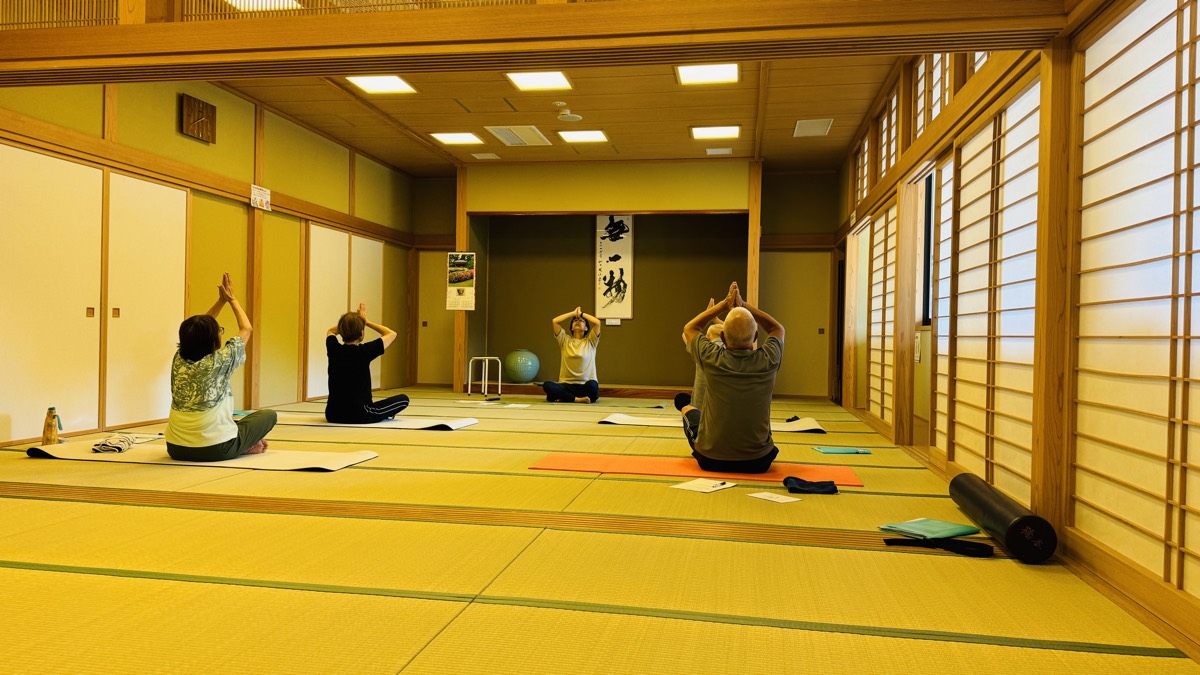 畳の大広間で腕を上げるストレッチをするグループレッスン